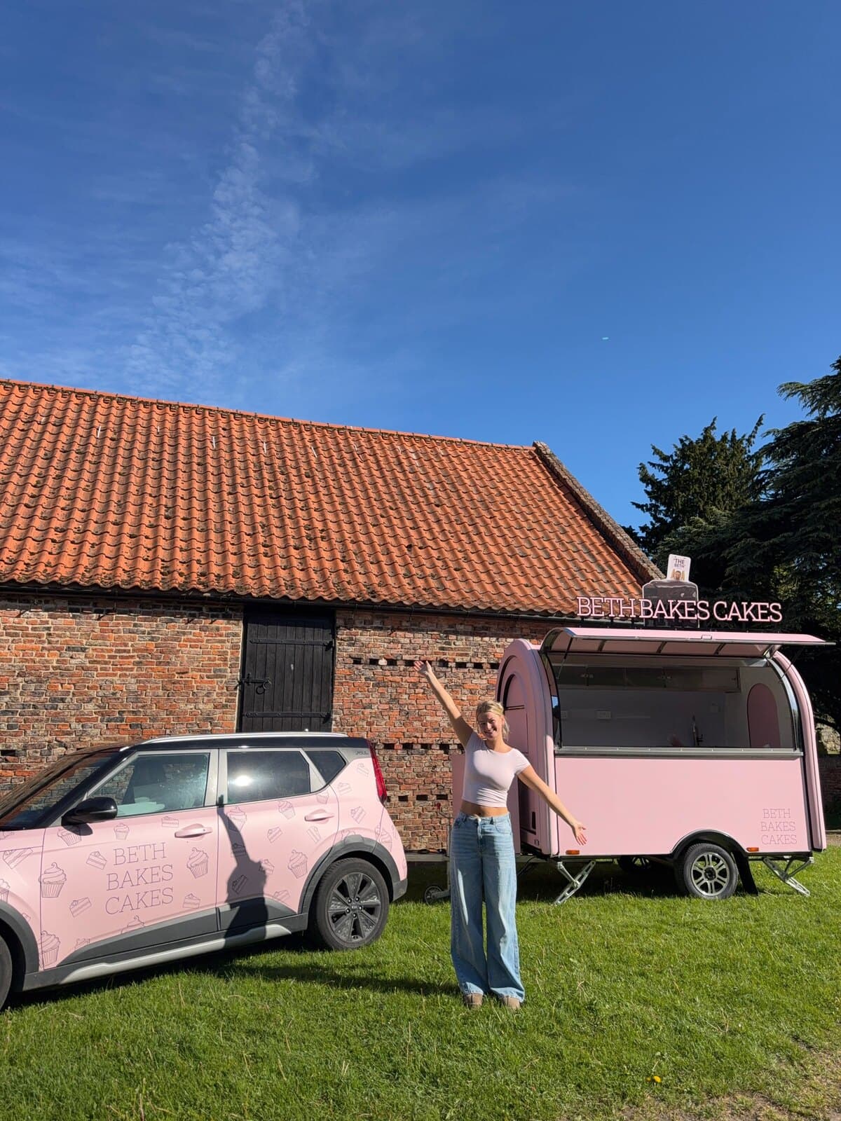 Beth in front of 'The Beth' pink trailer and her branded car
