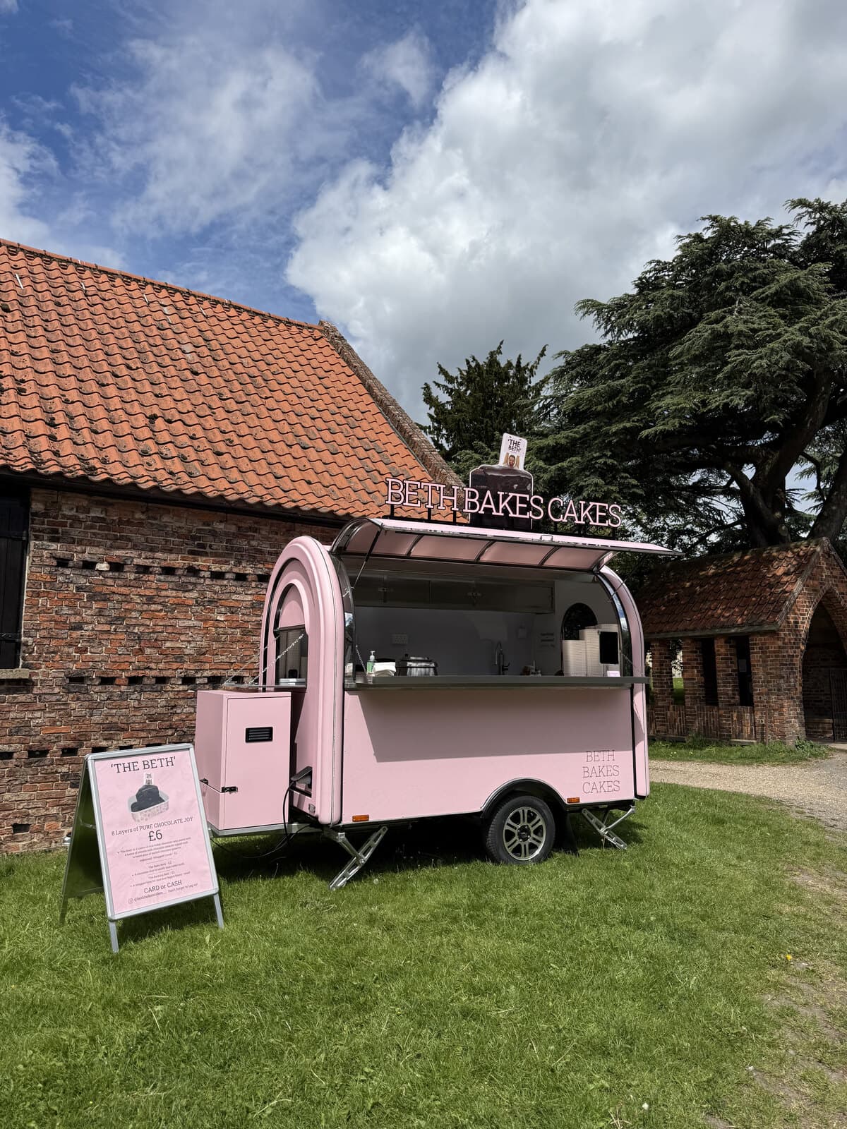 'The Beth' pink trailer bar parked beside a brick barn with its menu board out front